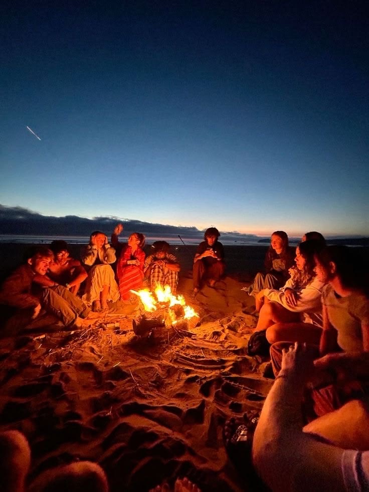 Friends gathered around a beach bonfire at sunset